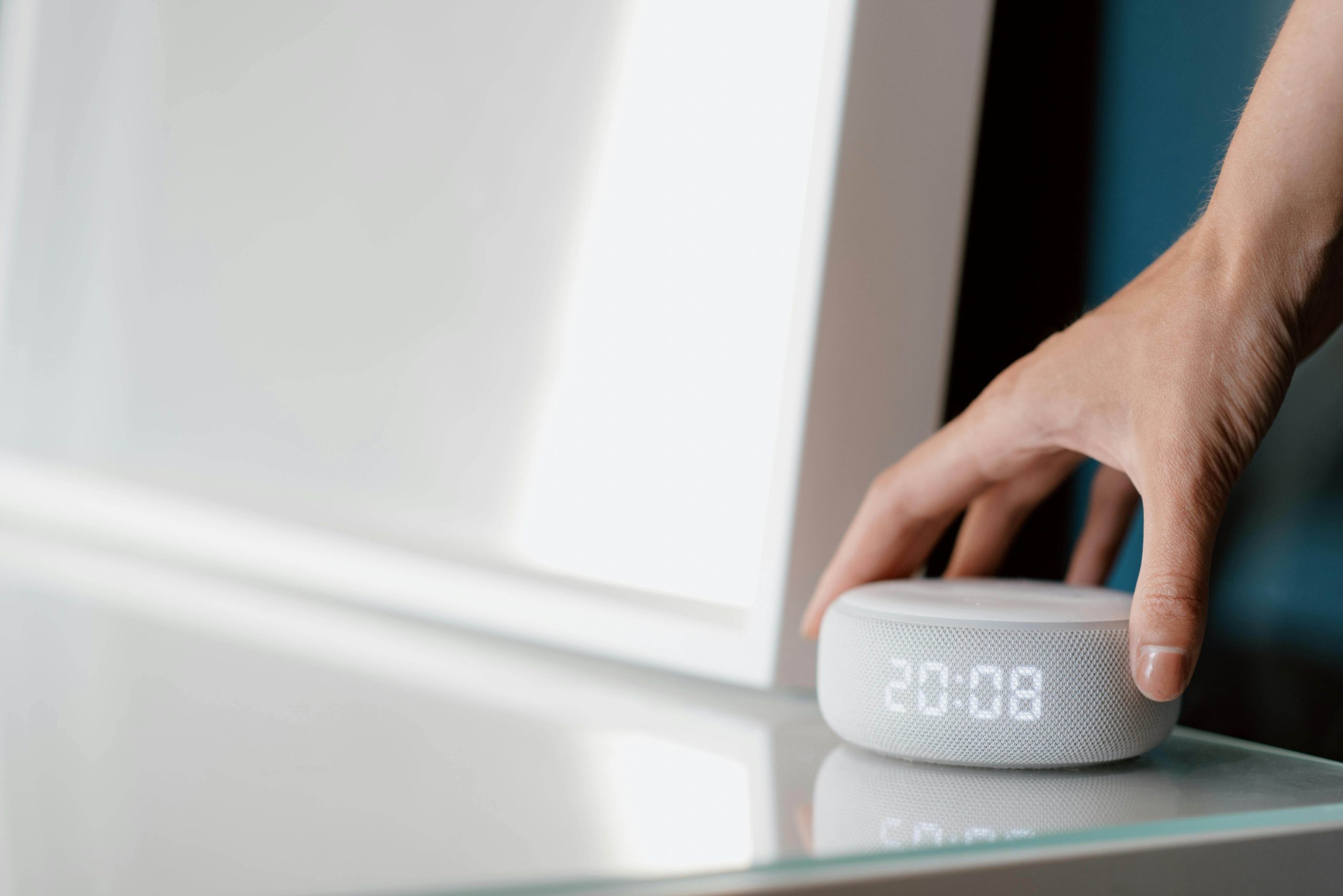 A person picking up a grey Voice User Interfaces (VUI) device from a glass table. A person picking up a grey Voice User Interfaces (VUI) device from a glass table.