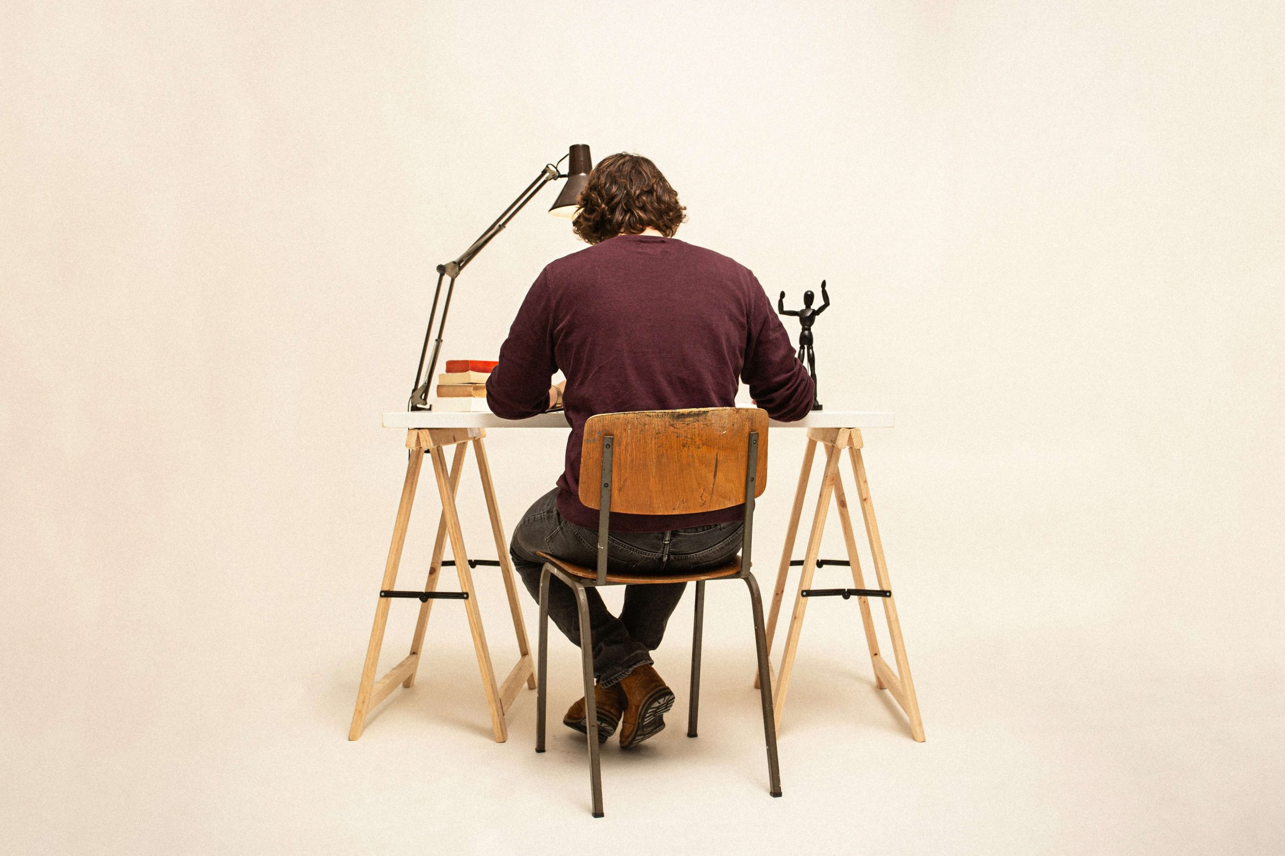 A man in a brown jumper sitting on a wooden chair, working at a desk. A man in a brown jumper sitting on a wooden chair, working at a desk.