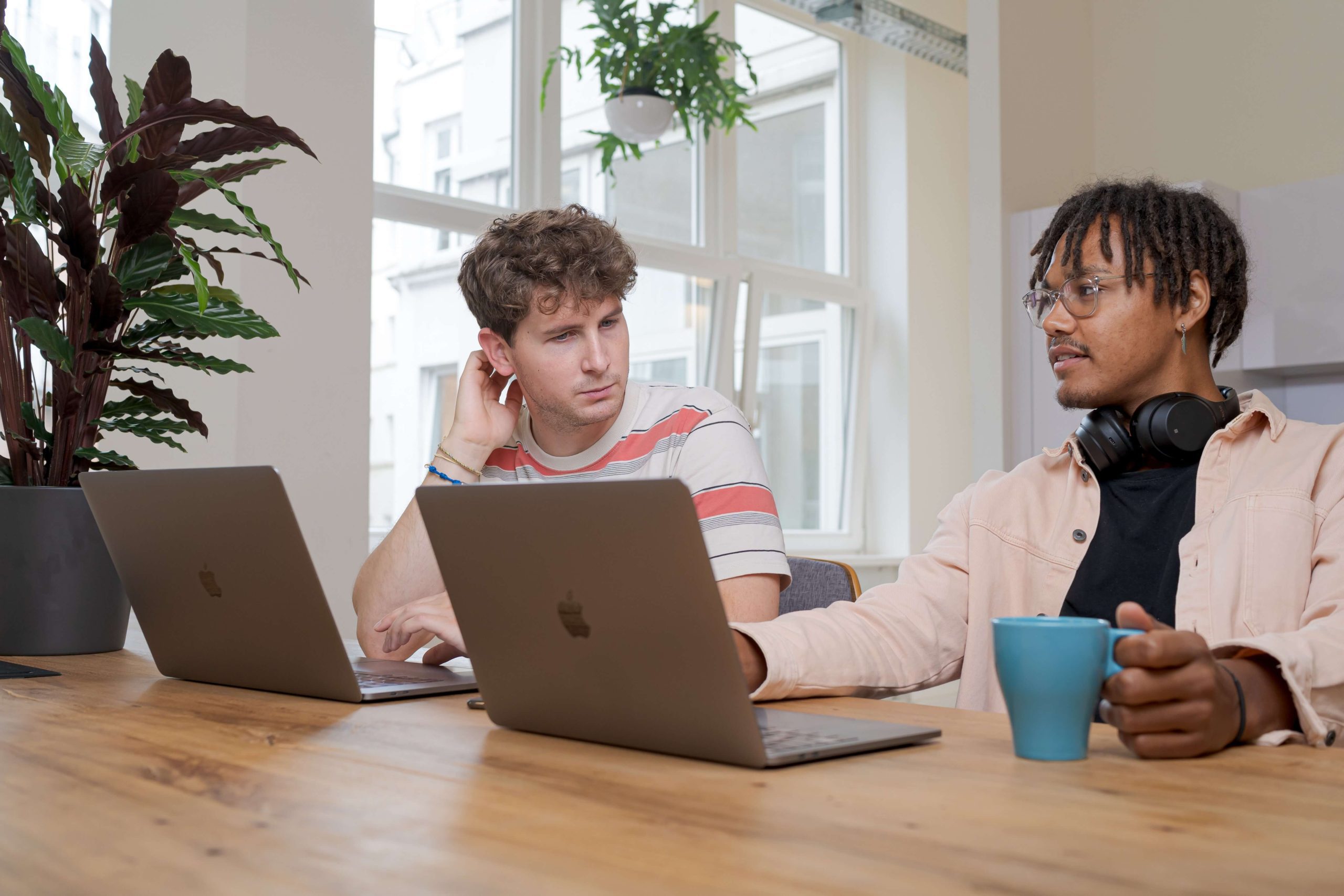 Two men sitting down with their laptops open in front of them, and talking to each other. Two men sitting down with their laptops open in front of them, and talking to each other.