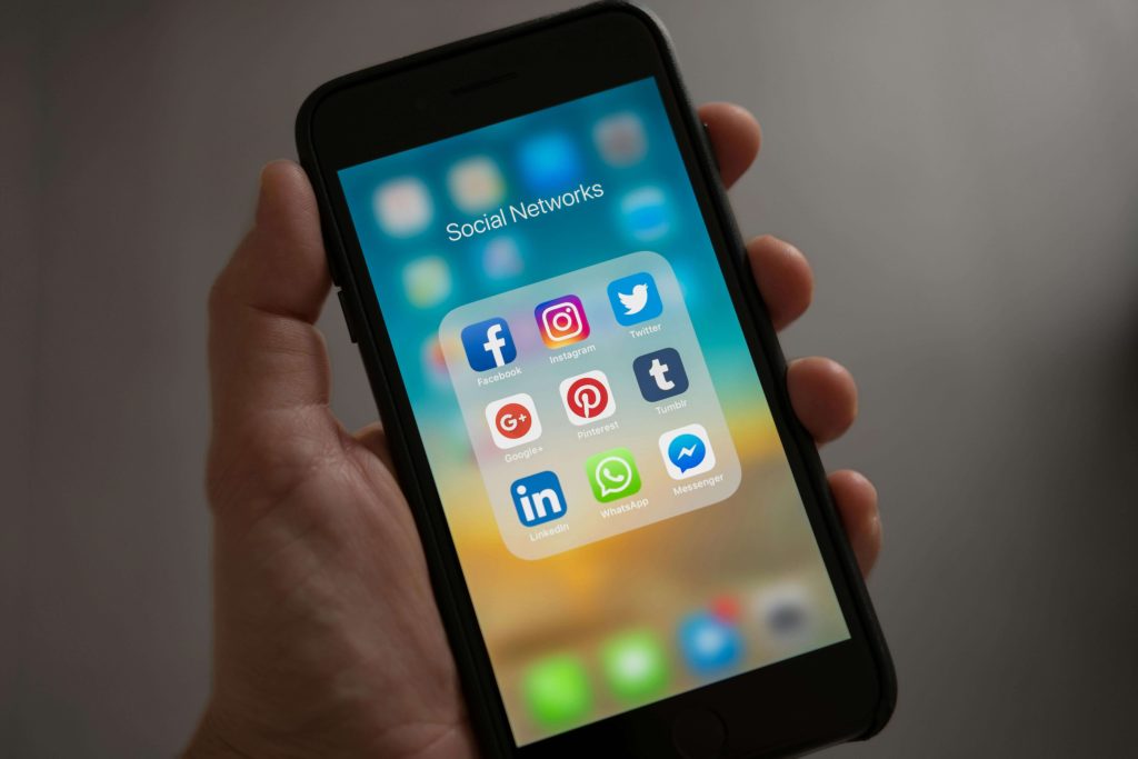 A person holding a phone with their left hand. The phone is opened to an apps folder called "Social Networks", featuring the app logos of Facebook, Instagram, and Pinterest.