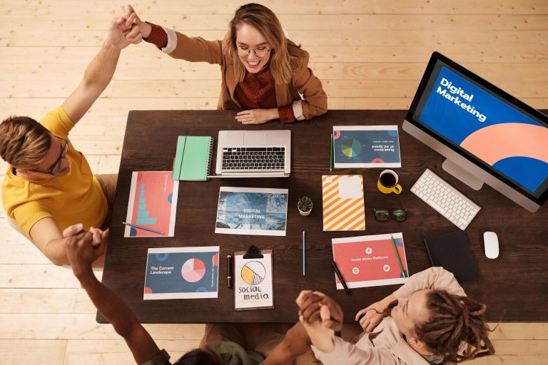 Four people are sitting around a table, with a computer screen reading "Digital Marketing" on a screen.