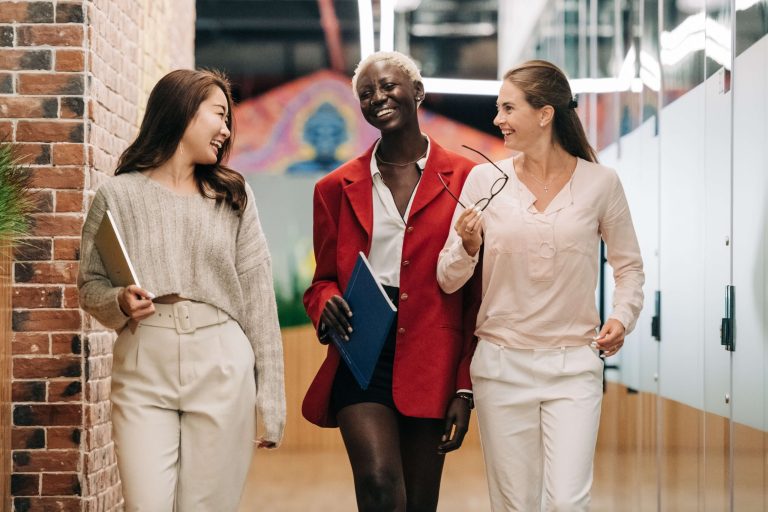 A group pf three women from different backgrounds, walking and smiling at each other.