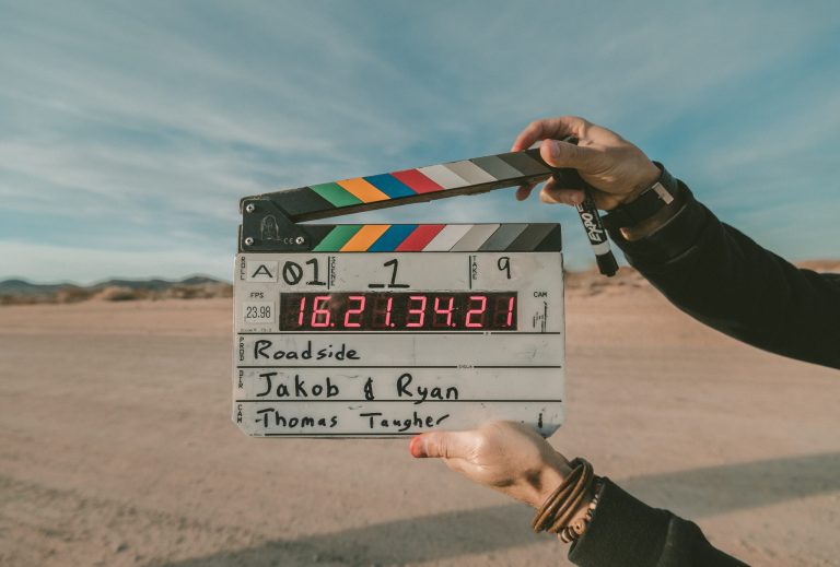 A person holding a C clapper board behind a desert background.
