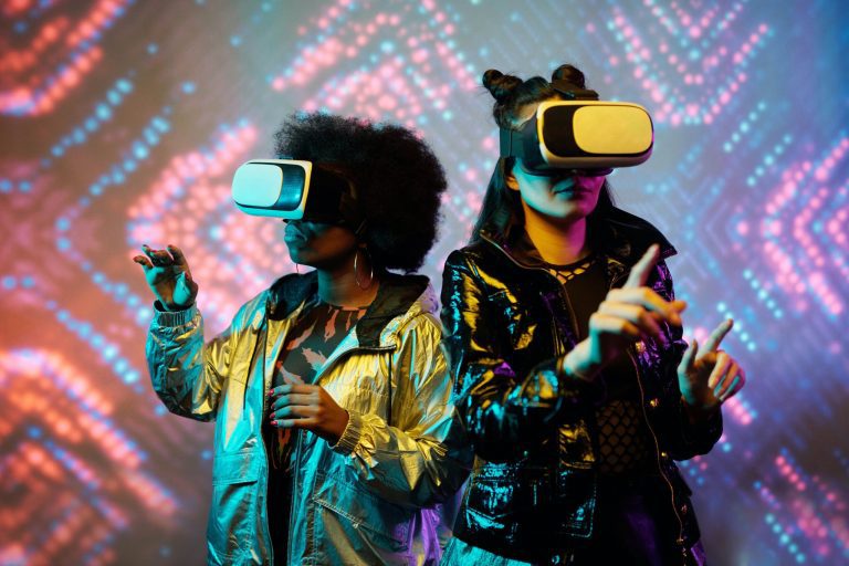 Two women wearing virtual reality googles, standing in front of a kaleidoscope background.