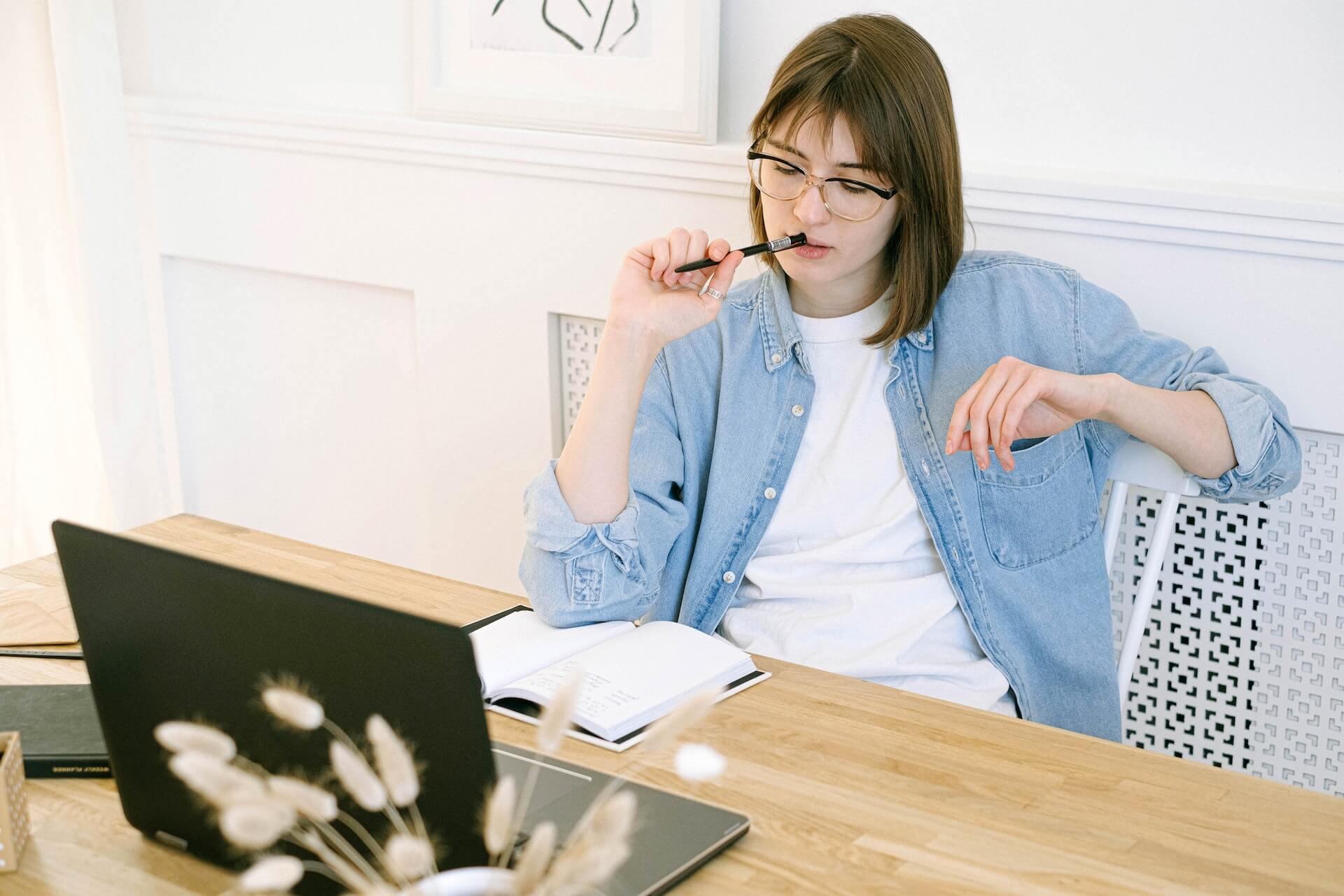 A woman sitting at a desk, in front of a laptop, holding a pencil.