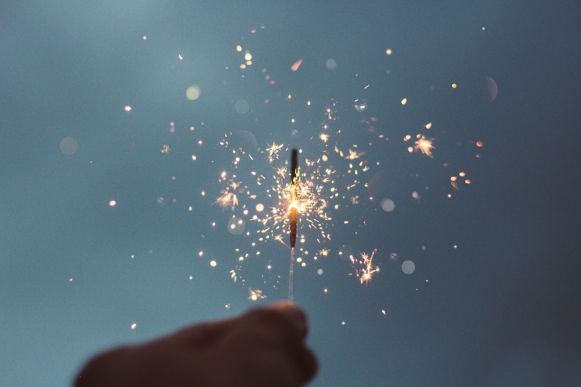 A person holding a lit sparkler in front of a blue background.