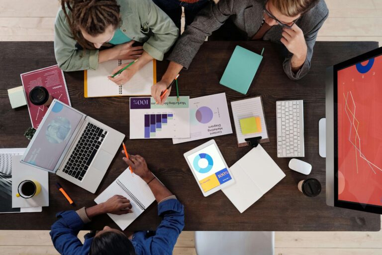A bird's eye view of three people working with printed graphs scattered over the table.