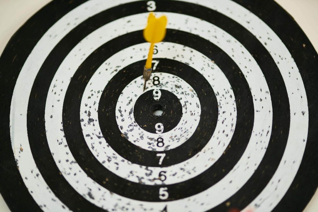 A black and white dartboard with a yellow dart on the penultimate circle to illustrate that businesses should focus on their audience.