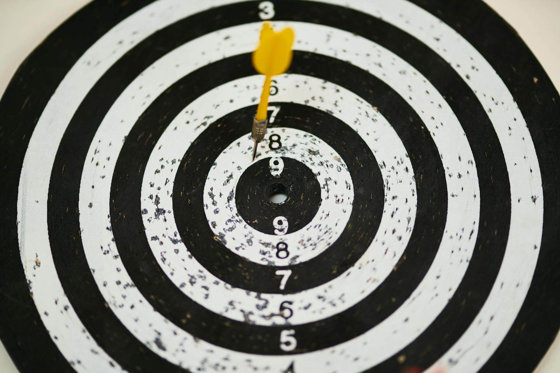 A black and white dartboard with a yellow dart on the penultimate circle to illustrate that businesses should focus on their audience.