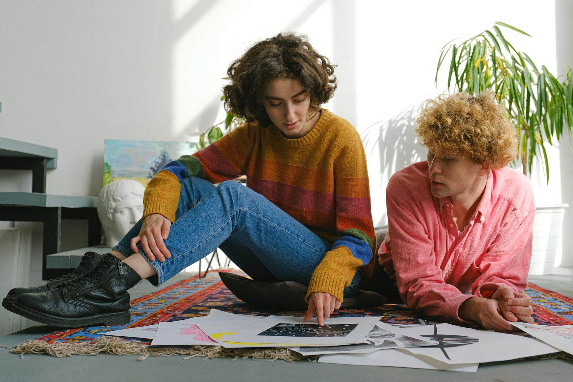 Two artists sitting on the floor, with multiple sheets of paper fanned out in front of them.