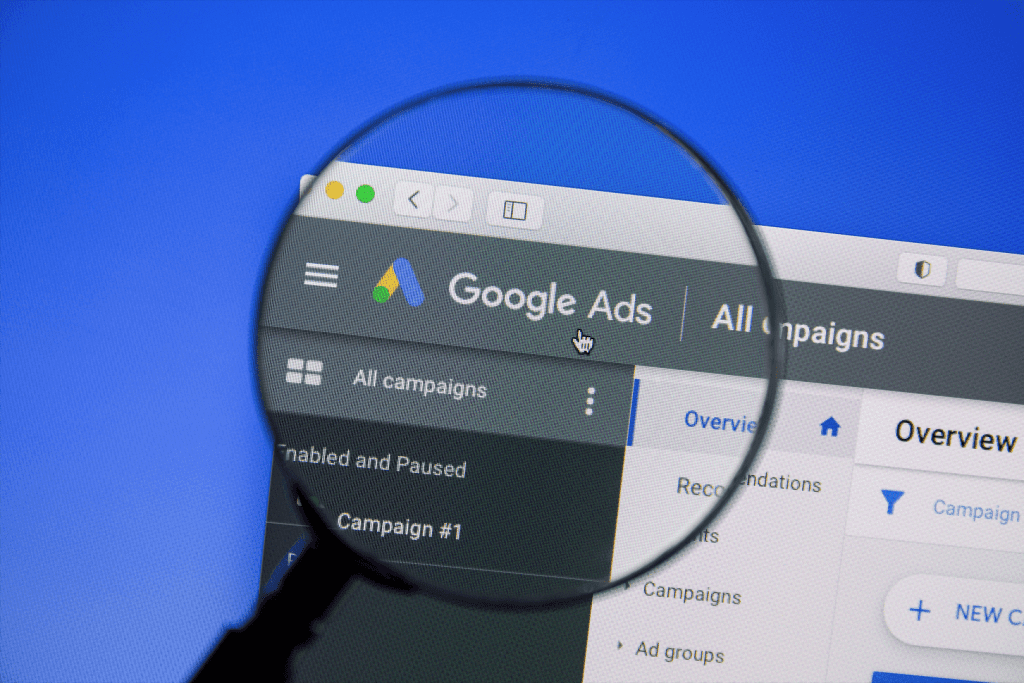 An image of the Google Ads dashboard on a screen and a magnifying glass zooming in the left corner of the dashboard.