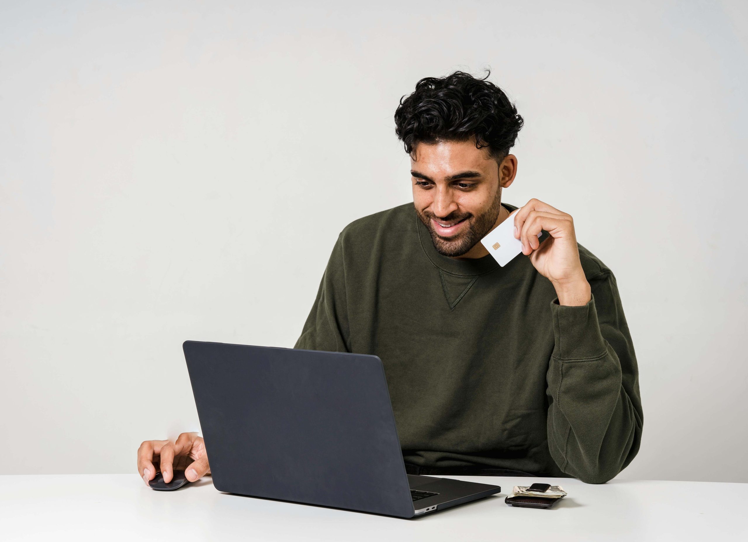 A man sitting down in front an opened laptop and holding a credit card with his left hand.