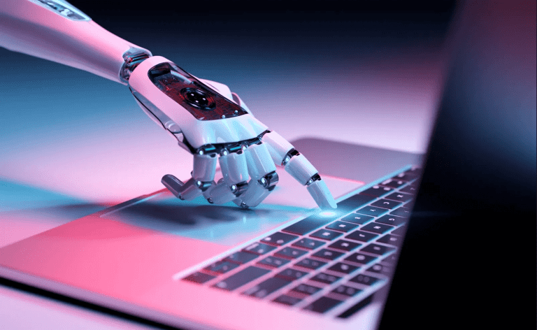 A white robotic hand touching the space bar of a laptop on a table, to signify the rise of AI chatbots.
